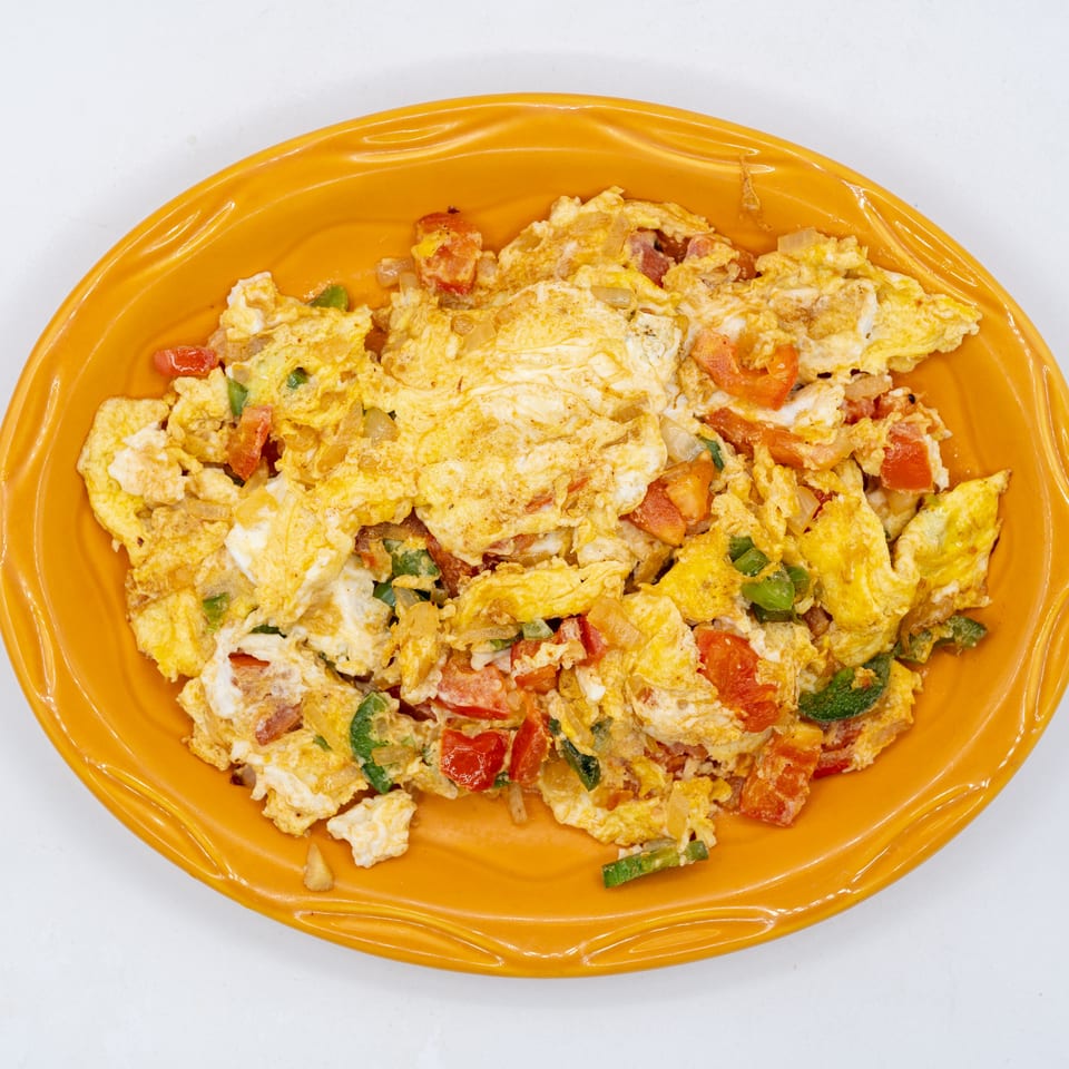 Scrambled eggs with tomatoes, green peppers, onions, and cheese served on an orange oval plate.