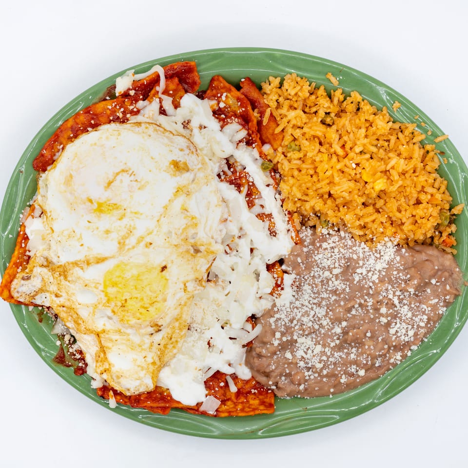 Mexican breakfast platter with fried eggs, red-sauced tortillas, Mexican rice, and refried beans topped with cheese.