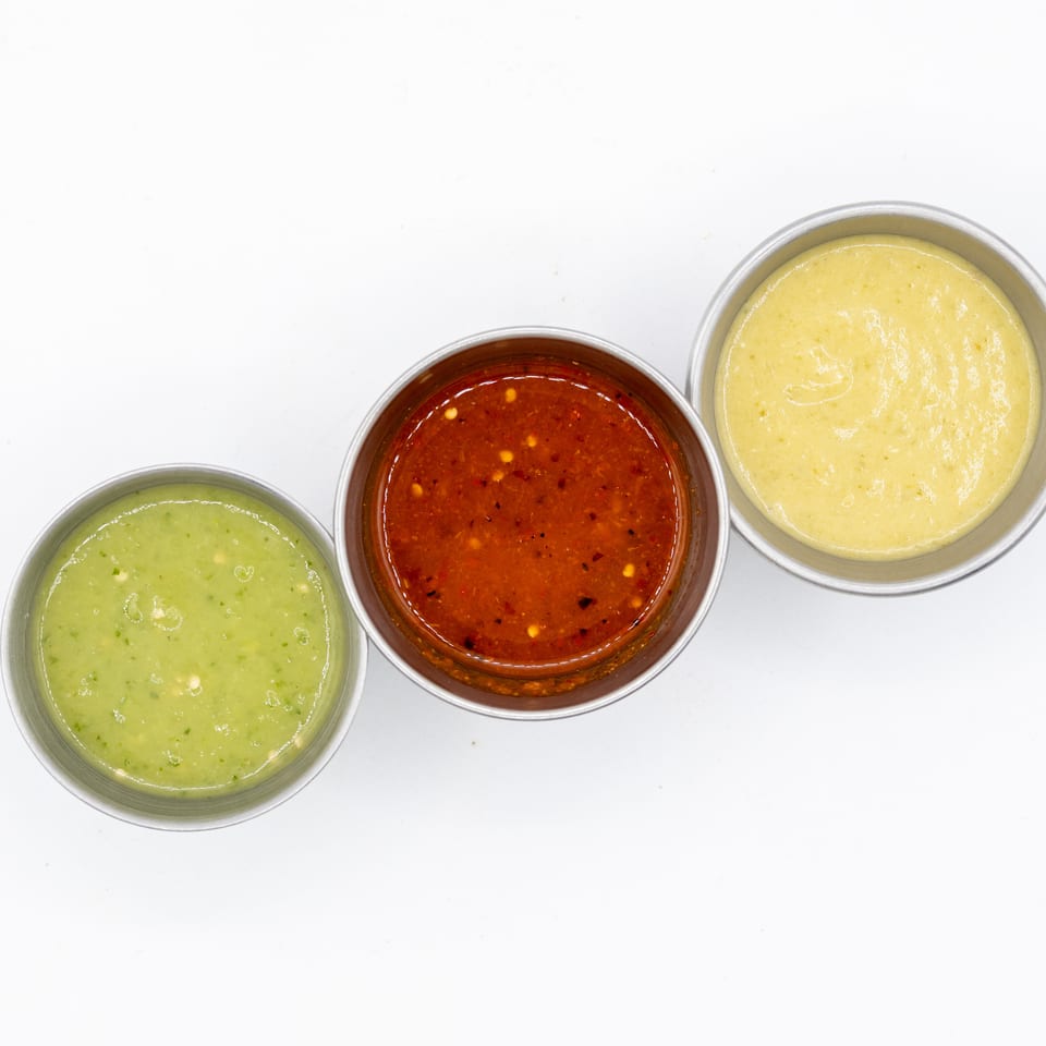 Three metal bowls of green, red, and yellow dipping sauces arranged on a white surface.