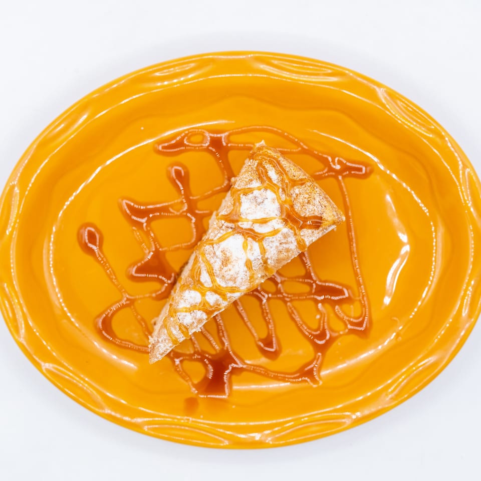 Triangular pastry dusted with powdered sugar and drizzled with caramel on an orange plate.
