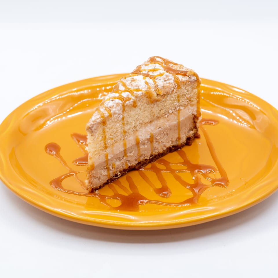 Slice of layered cake dusted with powdered sugar and drizzled with caramel sauce on an orange plate.