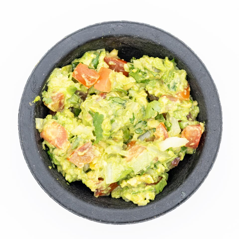 Fresh chunky guacamole with tomatoes, onions, and cilantro served in a black bowl.