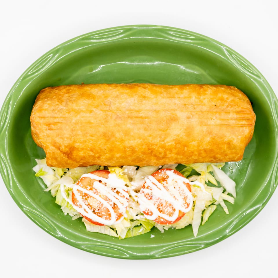 Golden-brown pastry served on shredded lettuce with sliced tomatoes and creamy dressing on a green plate.