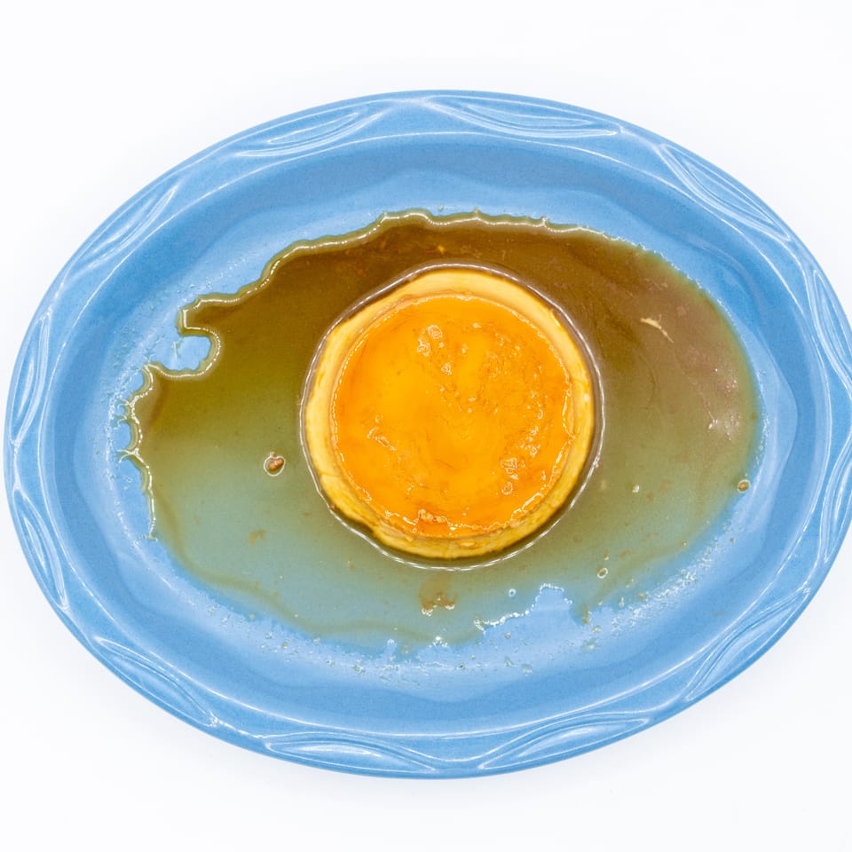 Caramel flan centered on a blue ceramic plate, surrounded by glossy caramel sauce.