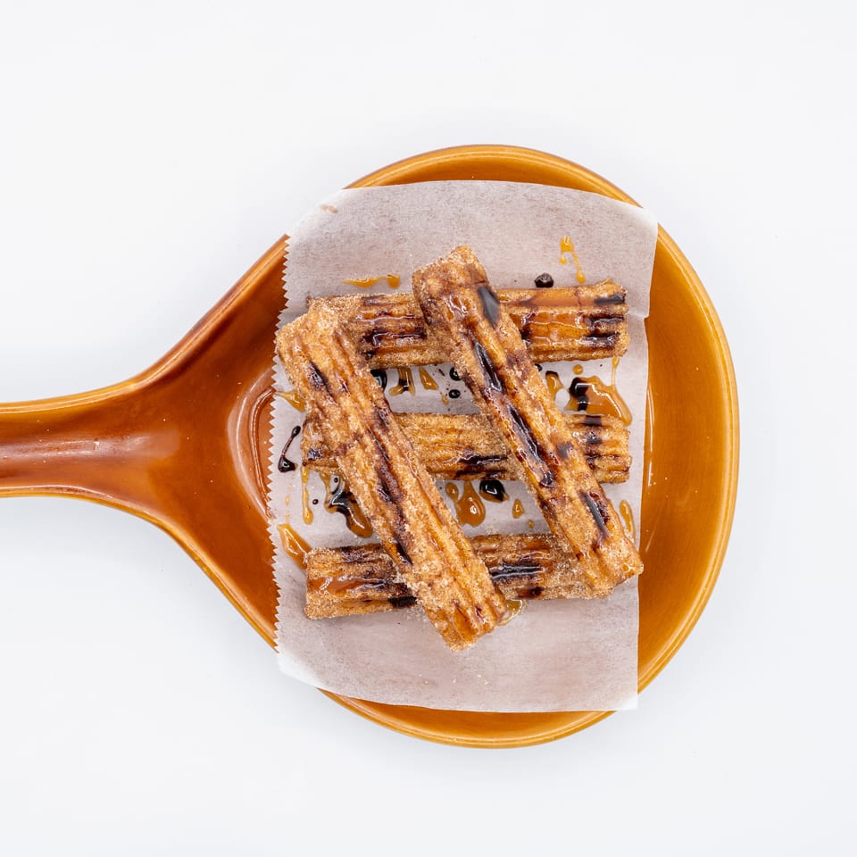 Crispy churro strips drizzled with chocolate and caramel sauce on parchment atop a brown ceramic plate.