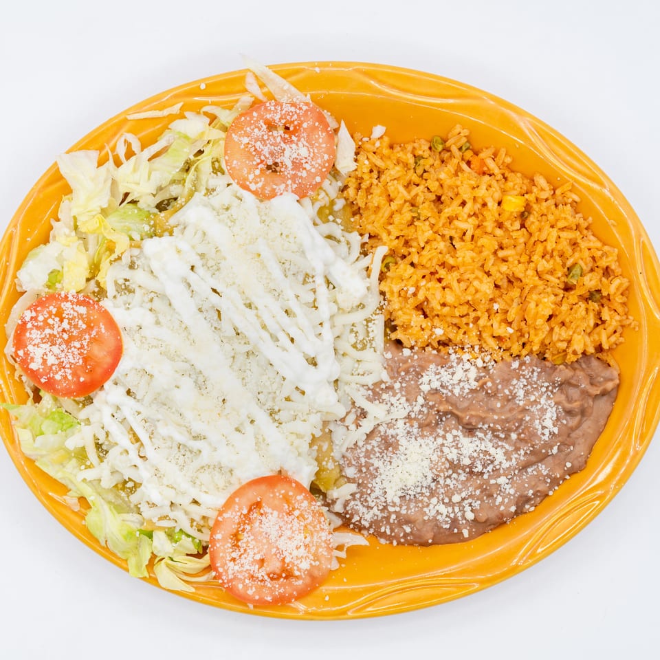 Mexican platter with rice, refried beans, lettuce salad, tomatoes, shredded cheese, and creamy sauce on an orange plate.
