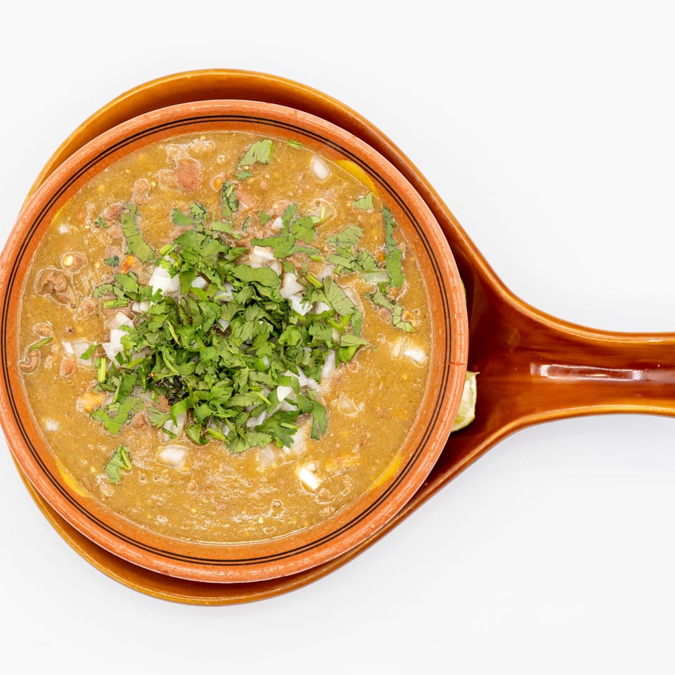 Overhead view of a savory soup garnished with chopped cilantro and onions in a terracotta bowl with handles.