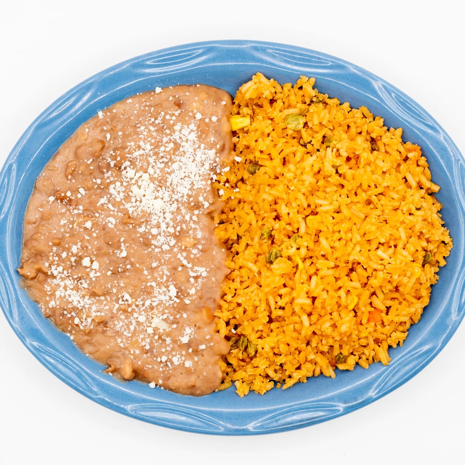 Refried beans topped with crumbled cheese and orange Mexican rice with vegetables on a blue oval plate.