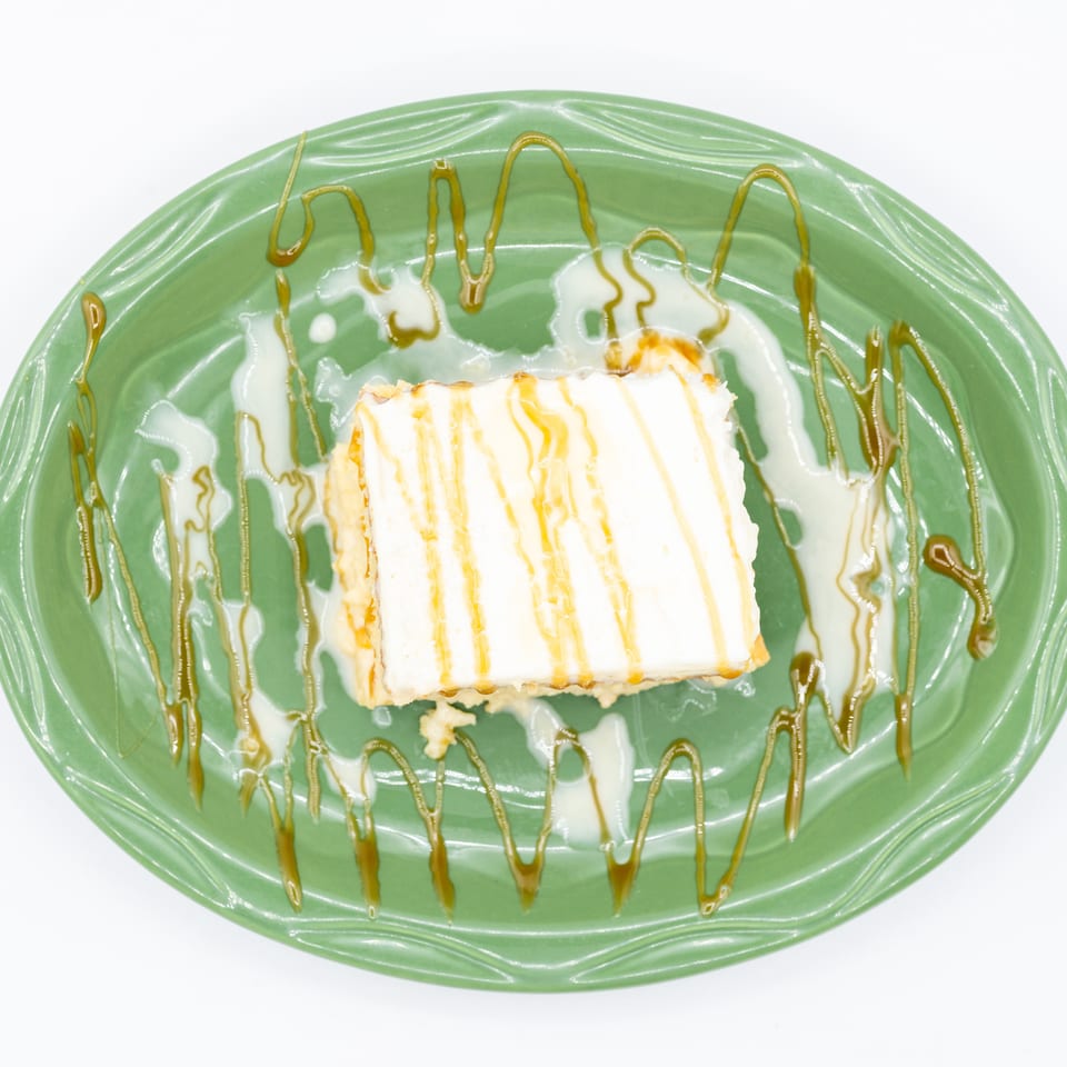 Rectangular layered dessert drizzled with caramel and cream sauce on a green decorative plate.