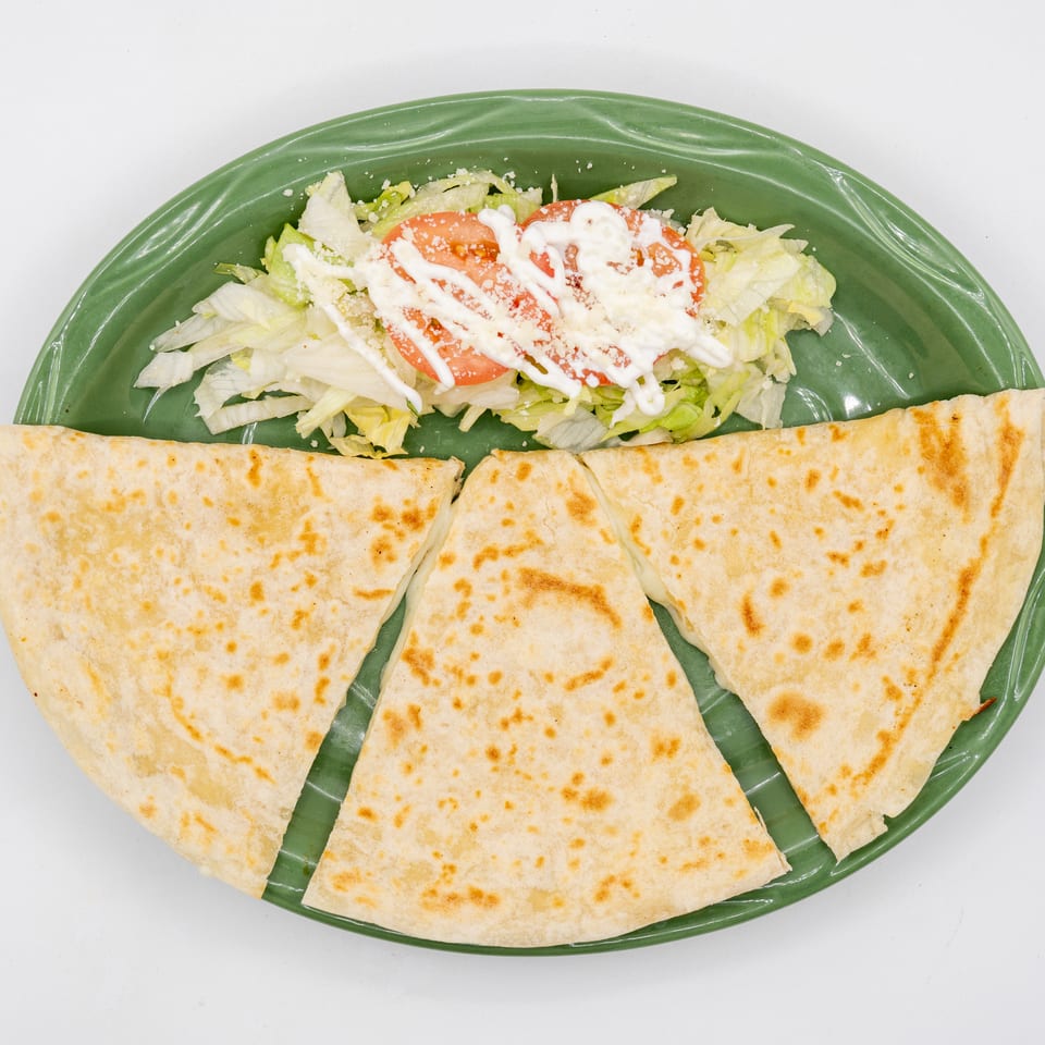 Grilled quesadilla wedges arranged on a green platter beside lettuce and tomato salad topped with creamy dressing.